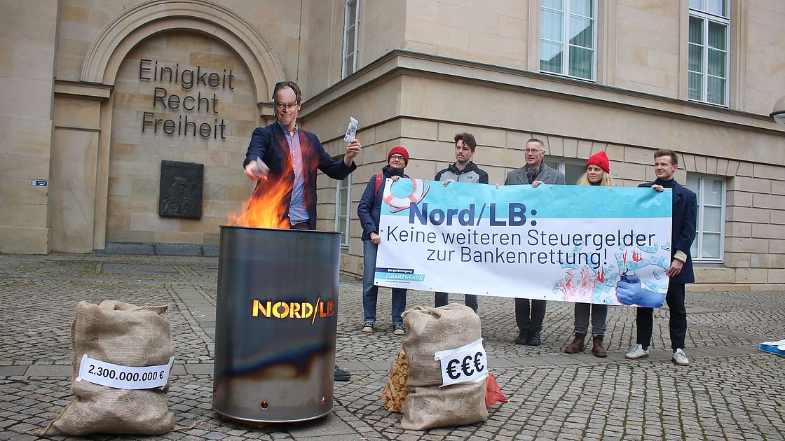 Mitglieder der Finanzwende Wende verbrennen Spielgeld in einer Feuertonne auf der Nord LB steht.